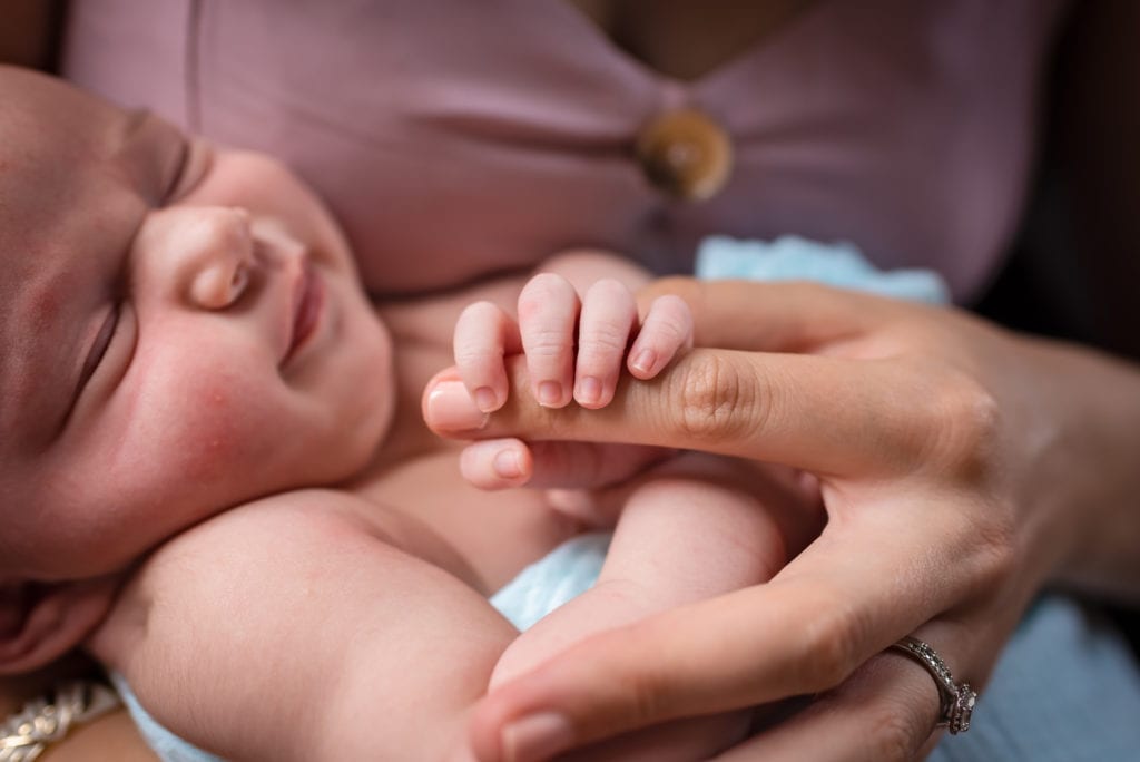 Newborn baby wrapping fingers around mom's fingers for newborn lifestyle in home photography session in los angeles