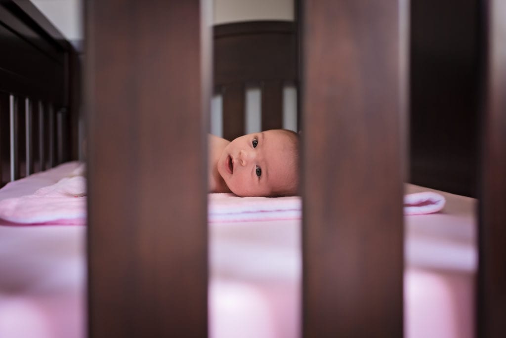 Baby in crib with pink sheets in home newborn pictures in los angeles