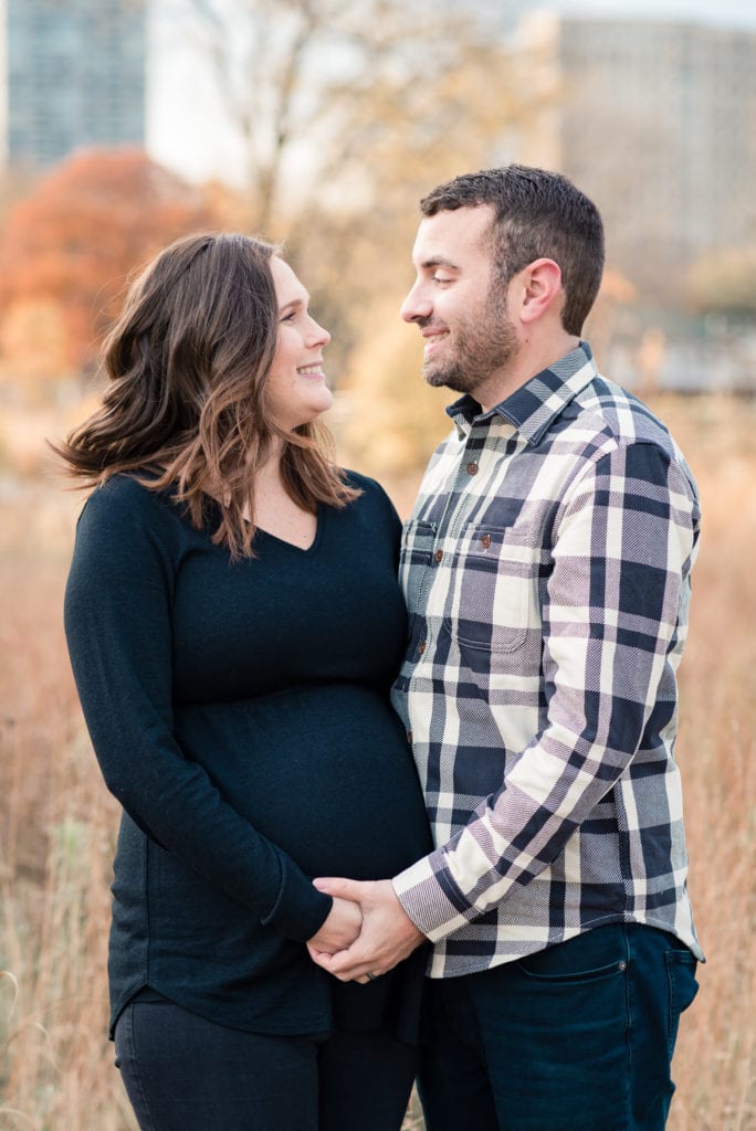 Husband and wife holding hands and looking at each other smiling during maternity pictures in Lincoln park nature boardwalk