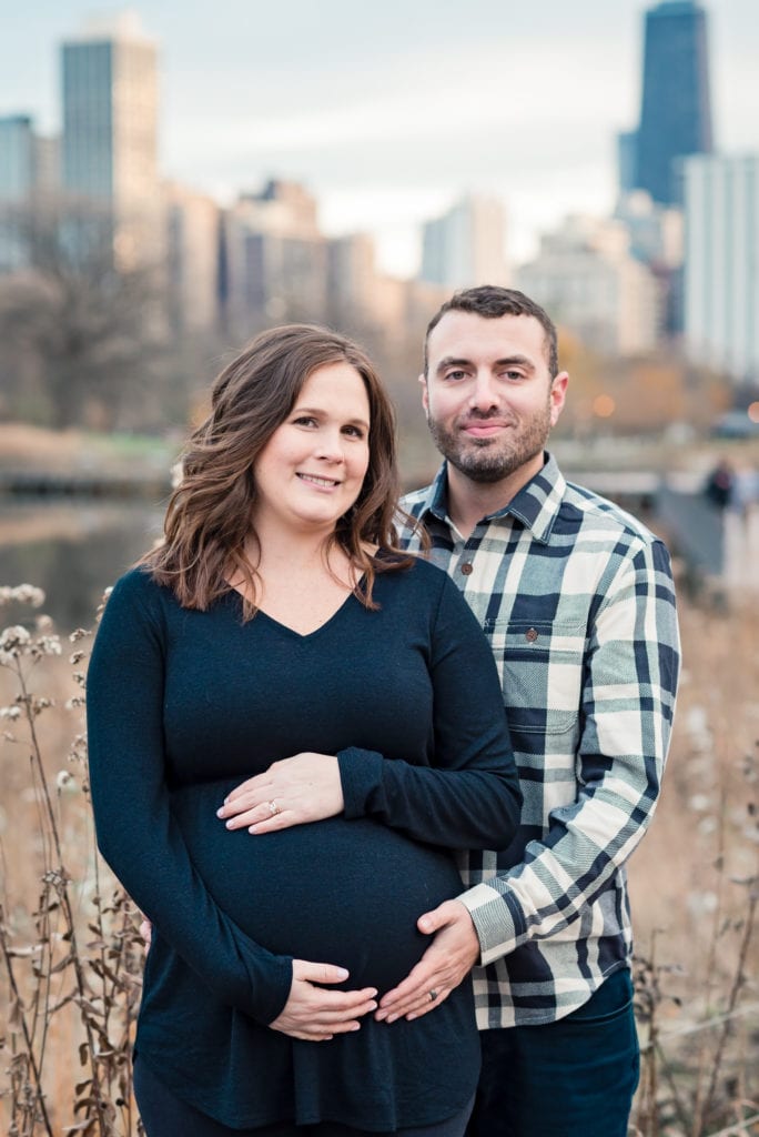 husband and wife smiling at camera in chicago during maternity photo shoot at Lincoln park nature boardwalk