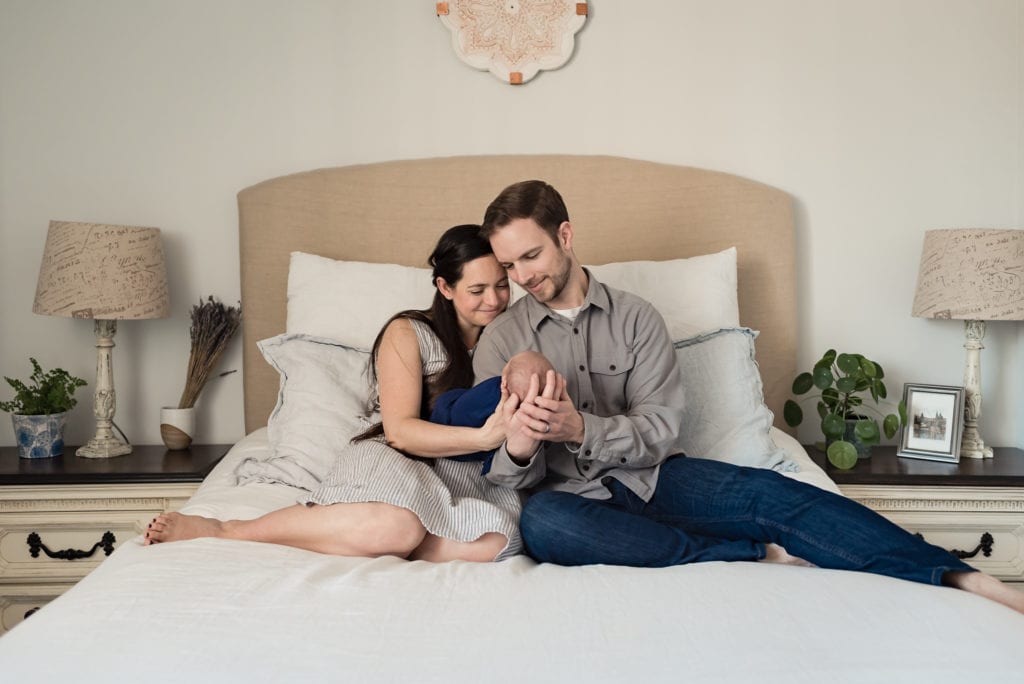 mom and dad sitting on bed holding baby los angeles newborn lifestyle photography session