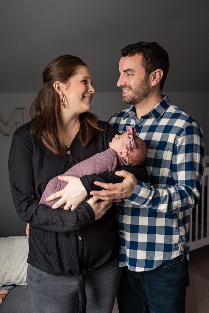 mom and dad smiling at baby while standing West Hollywood Newborn Pictures