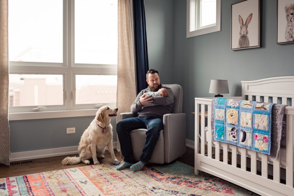 Culver City Newborn Pictures dad holding baby in nursery with dog looking up at them